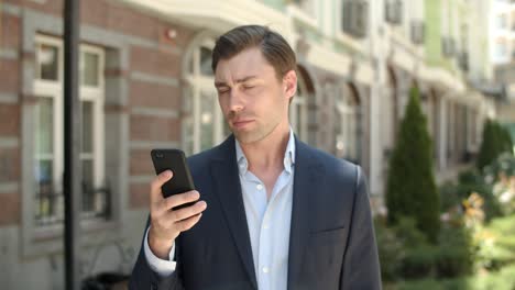 Portrait-man-using-smartphone-outdoor.-Businessman-typing-on-phone-at-street