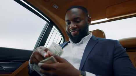 Closeup-african-man-smelling-dollars-at-car.-Man-sitting-with-money-at-vehicle