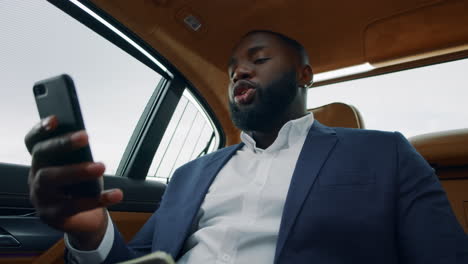Closeup-african-man-making-video-call-at-car.-Afro-man-shaking-money-at-backseat