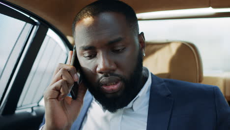Closeup-focused-african-businessman-talking-mobile-phone-at-luxury-car.