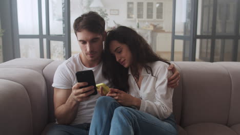 Happy-couple-sitting-on-sofa-with-mobile-phones-together.