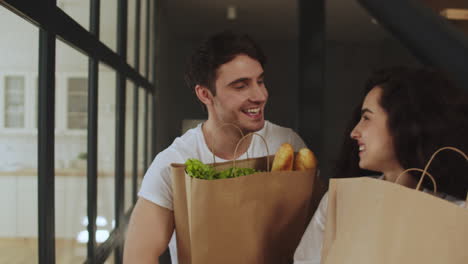 Happy-couple-walking-with-paper-bags-with-healthy-food.-Couple-hugging-at-home
