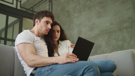 Portrait-of-scared-couple-looking-computer-screen-at-sofa-in-slow-motion.