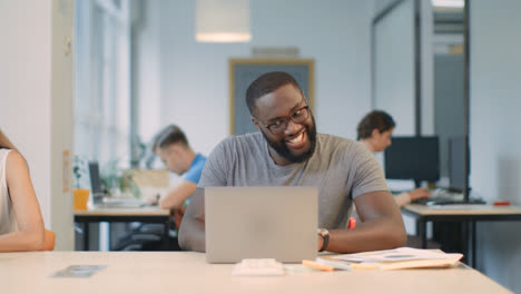 Glücklicher-Afrikanischer-Mann-Liest-Gute-Nachrichten-Auf-Laptop-Computer-Im-Coworking-Space