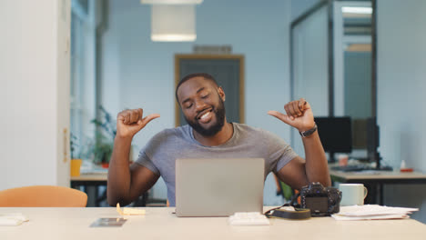 Happy-photographer-working-on-computer-at-coworking.-Black-man-looking-photos.