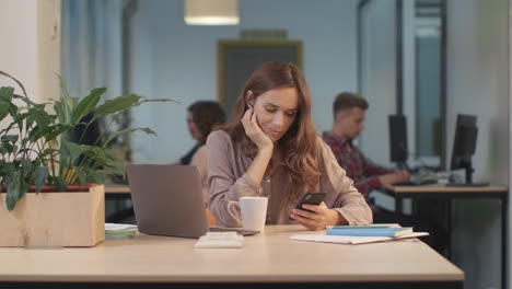 Tired-woman-scrolling-mobile-at-coworking.-Portrait-of-lady-chatting-on-phone