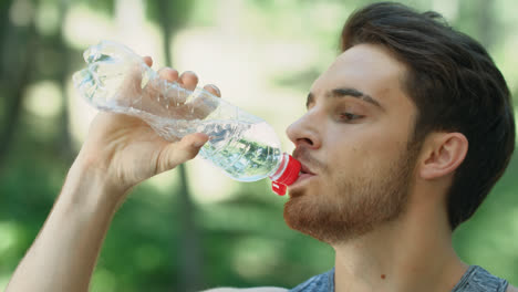 Thirsty-man-drinking-water-from-bottle-in-summer-park.-Portrait-of-sport-man