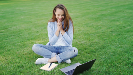 Happy-woman-working-on-laptop-computer-on-green-lawn-in-summer-park