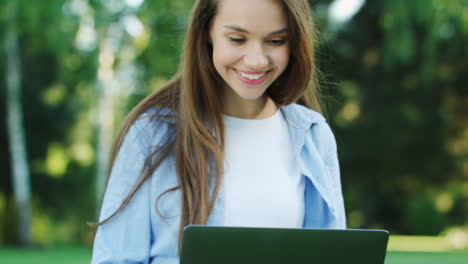 Smiling-woman-working-on-laptop-computer-in-city-park-at-summer-day
