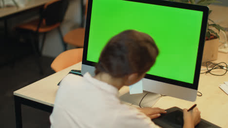 Young-woman-working-on-computer-with-green-screen-in-office.-Graphic-designer