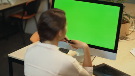 Young-woman-working-on-computer-with-green-screen-in-office