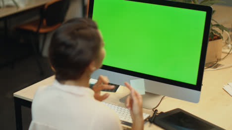 Young-woman-call-video-online-on-computer-with-green-screen-in-office
