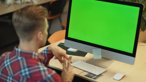 Young-man-call-video-online-on-computer-with-green-screen-in-office