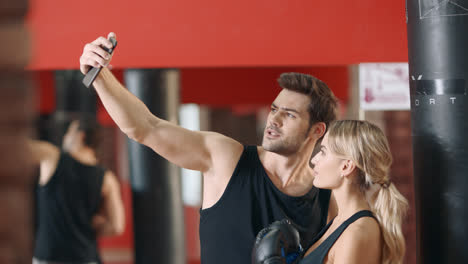 Happy-couple-making-selfie-in-fitness-gym.-Woman-and-man-taking-mobile-photo