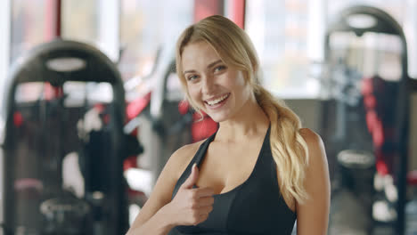 Portrait-of-trainer-female-showing-thumb-up-gesture-in-fitness-club.