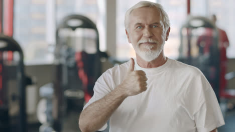 Smiling-elderly-man-showing-thumb-up-gesture-in-healthy-club.