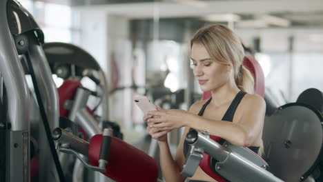 Fitness-woman-relaxing-with-mobile-phone-in-sport-gym.