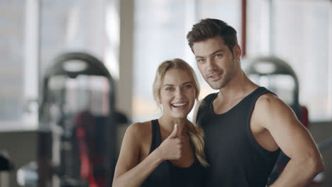 Happy-couple-posing-in-modern-gym.-Smiling-woman-showing-thumbs-up-gesture.