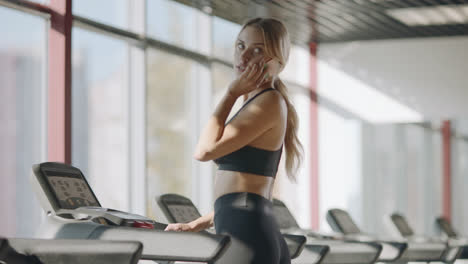 Slim-sport-woman-talking-mobile-phone-in-fitness-gym.-Fit-girl-walking-treadmill