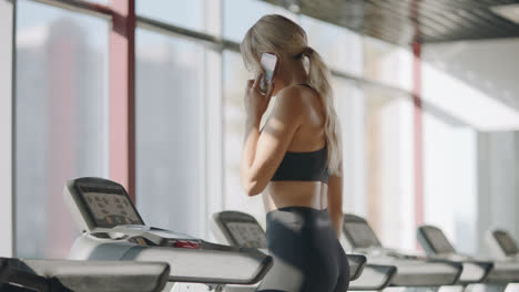 Fitness-woman-walking-on-treadmill-in-gym-club.-Pretty-girl-calling-mobile-phone