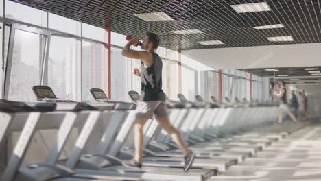Laufender-Mann-Trinkt-Wasser-Auf-Laufbandgerät-Im-Fitnessstudio.