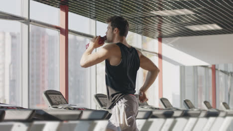 Runner-man-drinking-water-from-bottle-at-intensive-training-on-treadmill-machine
