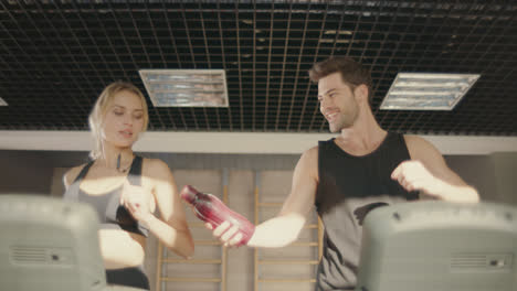 Handsome-man-flirting-with-woman-on-treadmill-machine-in-fitness-club.