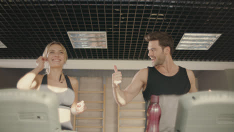 Joyful-fitness-couple-talking-on-treadmill-machine-in-gym-club.