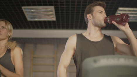 Young-man-drinking-water-on-treadmill-in-fitness-gym.