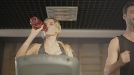 Smiling-male-runner-giving-drinking-bottle-to-fit-woman-in-fitness-gym.
