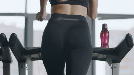 Back-view-sport-woman-training-leg-flexion-at-treadmill-in-fitness-gym.