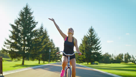 Happy-woman-enjoying-bicycle-ride-and-waving-hand-in-summer-park.-Riding-bicycle