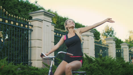 Cheerful-woman-bicyclist-enjoying-cycling-and-rising-up-hand-in-summer-park