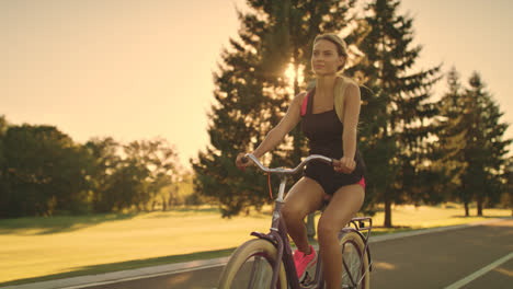 Mujer-Fitness-Montando-Bicicleta-En-El-Parque-De-Verano-En-El-Paisaje-Dorado-Del-Atardecer
