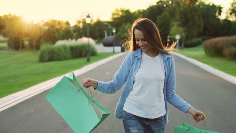 Happy-woman-holding-shopping-bag-walking-on-street-at-sunset