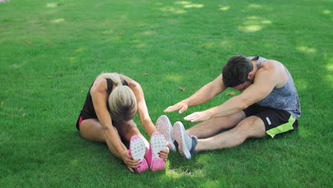 Junges-Paar-Dehnt-Sich-Vor-Dem-Fitnesstraining-Auf-Grünem-Gras-Im-Sommerpark