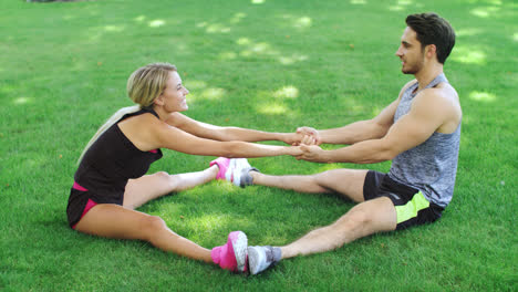 Happy-couple-man-and-woman-doing-stretching-exercise-on-grass-in-summer-park