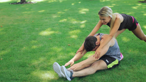 Woman-sport-trainer-help-fitness-man-stretching-legs-in-summer-park