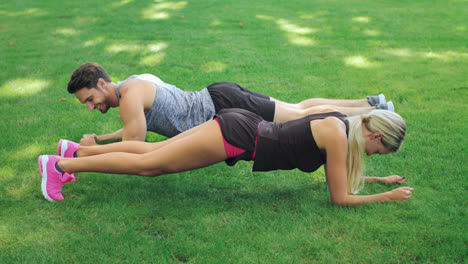 Fitness-couple-man-and-woman-training-plank-exercise-on-grass-in-summer-park