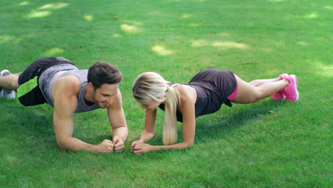 Athlete-man-and-woman-training-together-plank-exercise-on-lawn-in-summer-park.