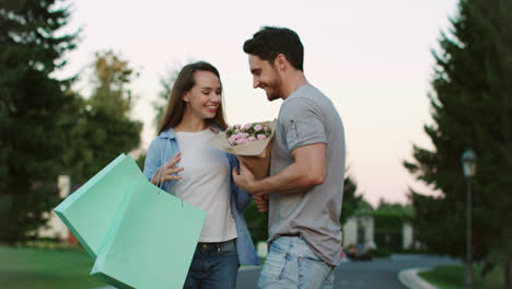 Smiling-woman-walking-on-city-street-and-meeting-boyfriend-with-flowers