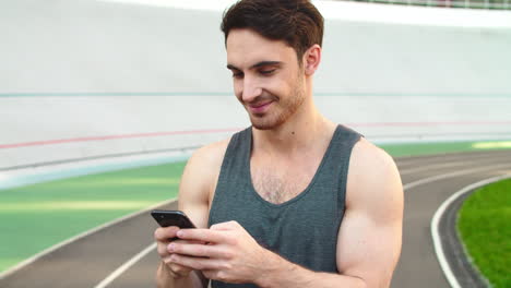 Closeup-runner-standing-with-smartphone-on-track.-Sporty-man-holding-phone