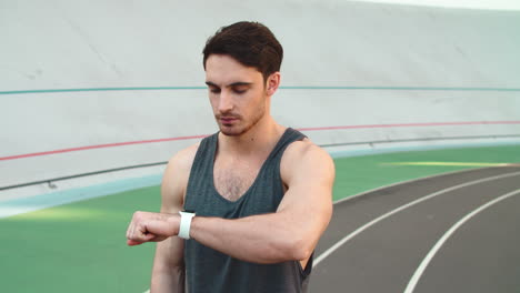 Man-runner-looking-on-smart-watch-at-stadium.-Young-jogger-checking-results