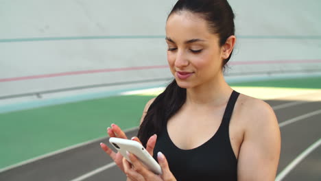 Sporty-girl-using-mobile-phone-at-stadium.-Ssport-woman-checking-results