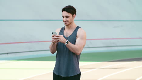Runner-man-using-mobile-phone-at-stadium-track.-Male-jogger-holding-phone