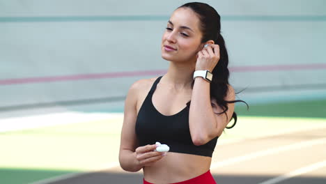 Sport-woman-wearing-earphones-at-modern-track.-Fit-woman-listening-music-outdoor