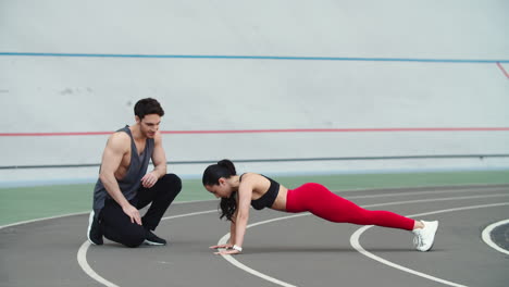 Woman-doing-push-ups-on-sport-stadium.-Couple-training-together-at-sport-stadium
