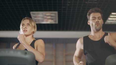 Concentrated-couple-running-together-on-treadmill-machine-in-gym-club.