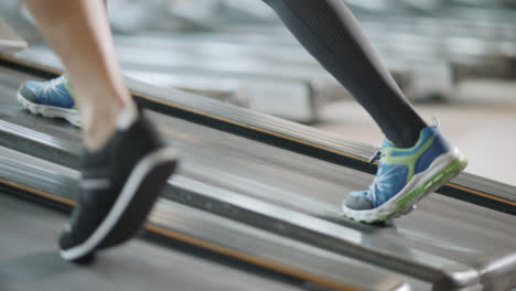 Closeup-two-pair-of-feet-moving-on-treadmill-in-fitness-gym.