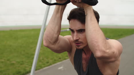 Close-up-fit-man-training-outdoors-with-trx-fitness-strap-at-stadium